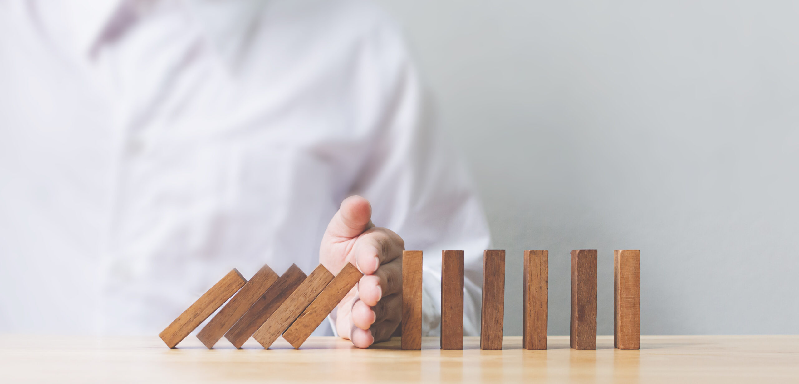 Hand stopping wooden domino business crisis effect or risk protection concept